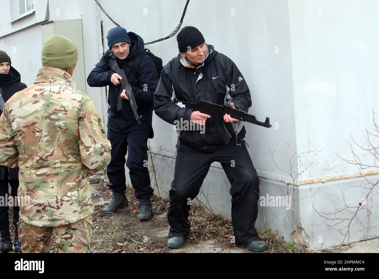 KHARKIV, UKRAINE - 19 FÉVRIER 2022 - deux hommes avec des découpes de fusil se cachent derrière un coin lors de l'exercice de défense territoriale pour les civils donné Banque D'Images