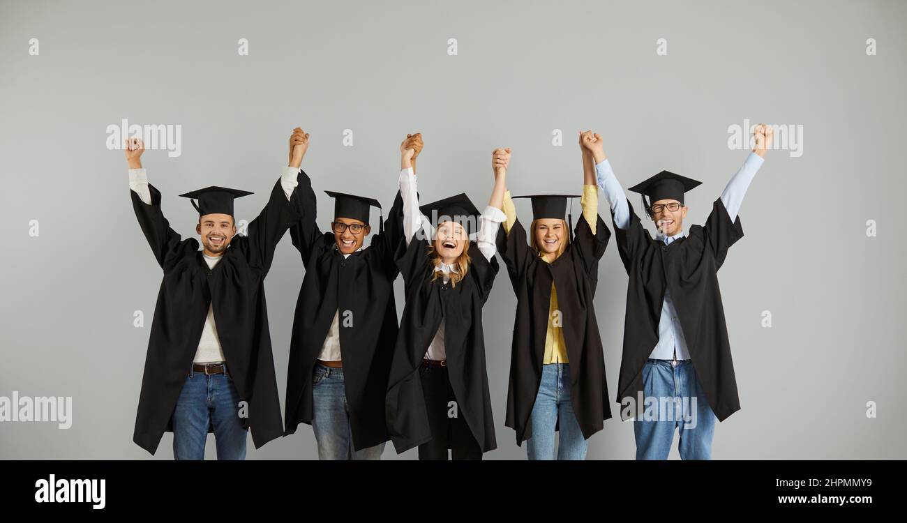 Portrait d'un groupe heureux et réussi de diplômés multiraciaux debout dans la rangée tenant les mains. Banque D'Images