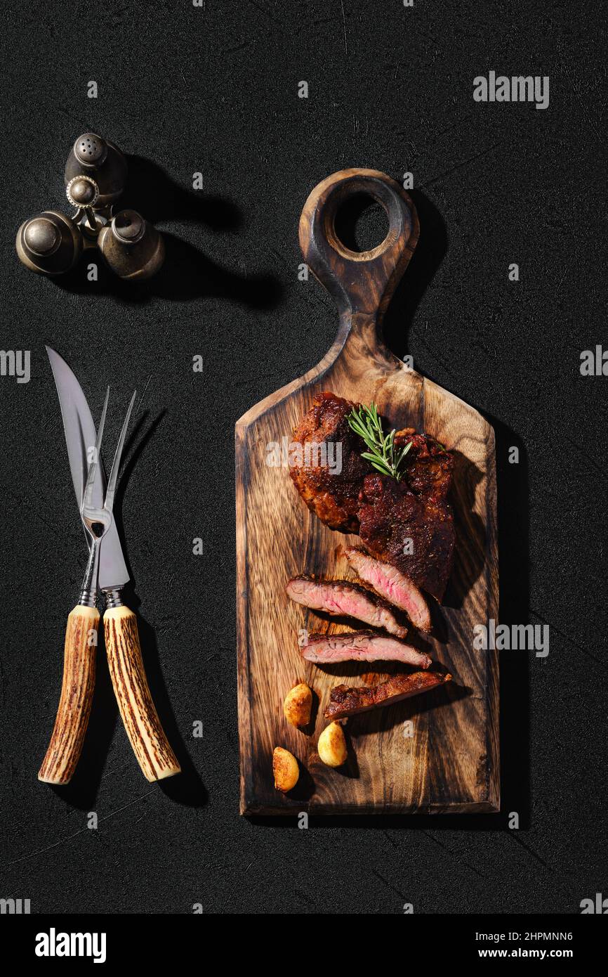 Vue en hauteur de l'araignée de beefsteak frite dans une poêle en fonte, servie sur une planche à découper en bois Banque D'Images