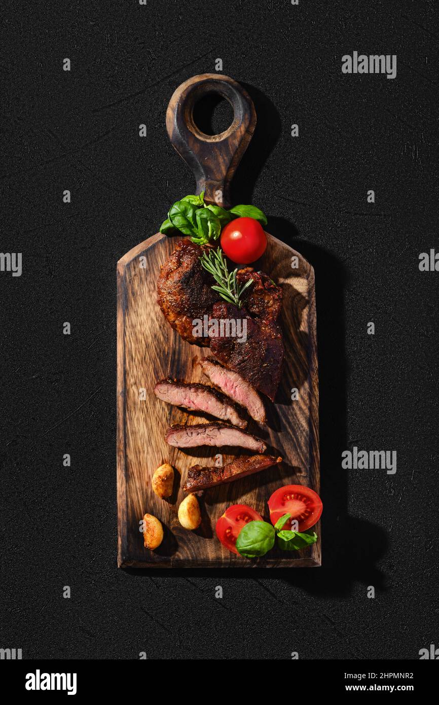 Araignée de beefsteak poêlée dans une poêle en fonte, servie sur une planche à découper en bois avec tomate et basilic Banque D'Images