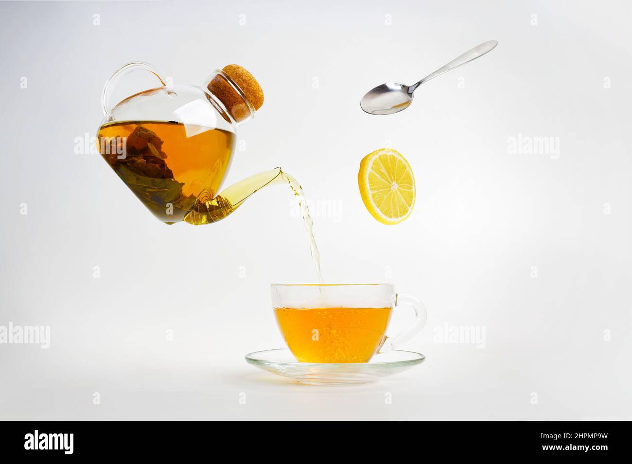 Le thé s'écoule d'une bouilloire transparente dans une tasse transparente. Une tranche de citron et une cuillère tombent Banque D'Images Le thé s'écoule d'une bouilloire transparente dans une tasse transparente. Une tranche de citron et une cuillère tombent Banque D'Images