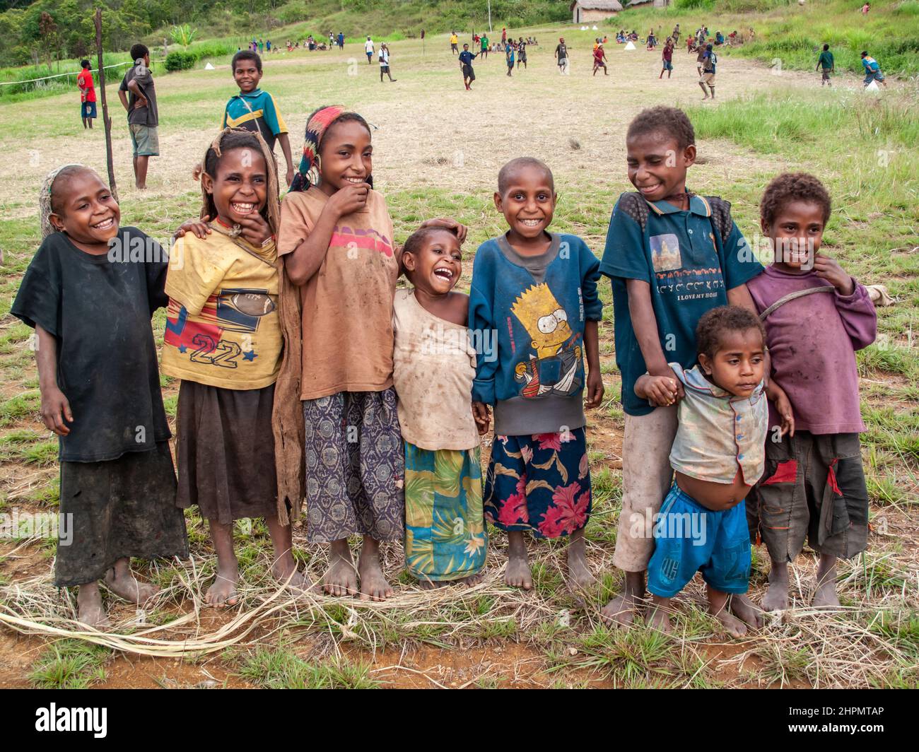 Huit enfants rient dans les montagnes de Papouasie-Nouvelle-Guinée avec un terrain de football derrière eux. Banque D'Images