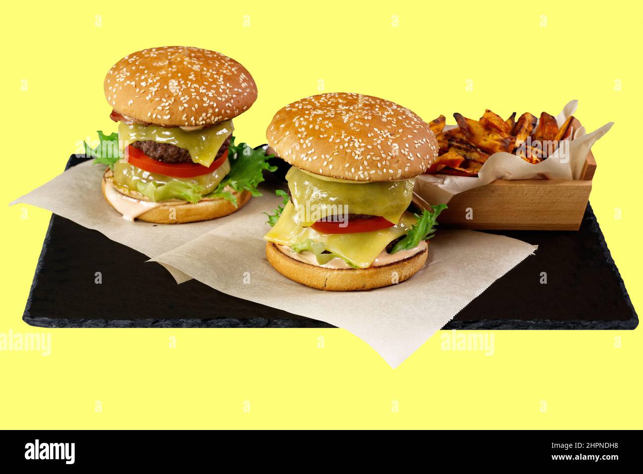 Deux gros hamburgers et patate douce isolés sur une assiette en pierre noire. Fond jaune Banque D'Images