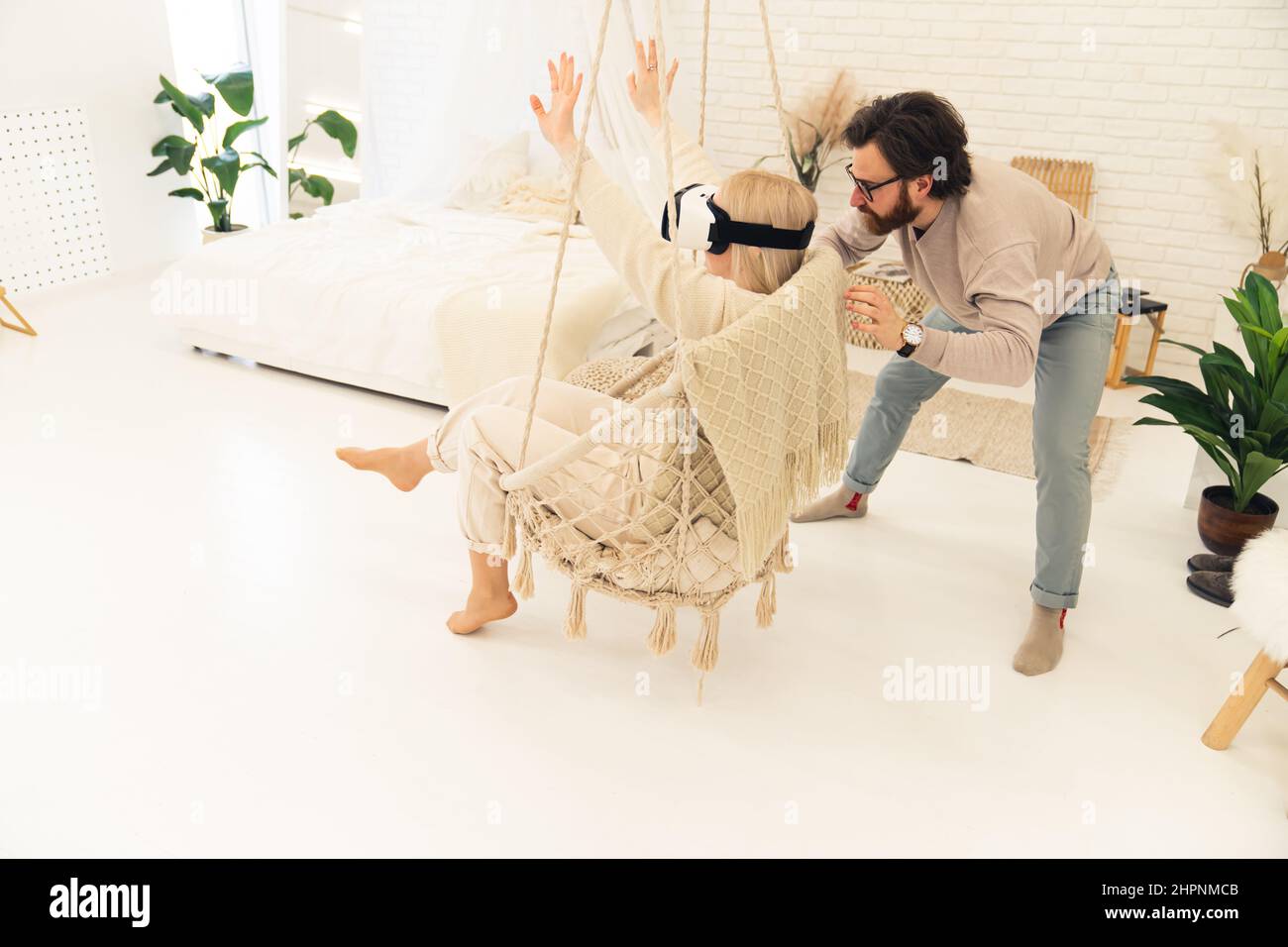 Jeune entrepreneur caucasien montrant sa fiancée aux cheveux blonds la technologie derrière les lunettes VR dans leur appartement moderne. Photo de haute qualité Banque D'Images