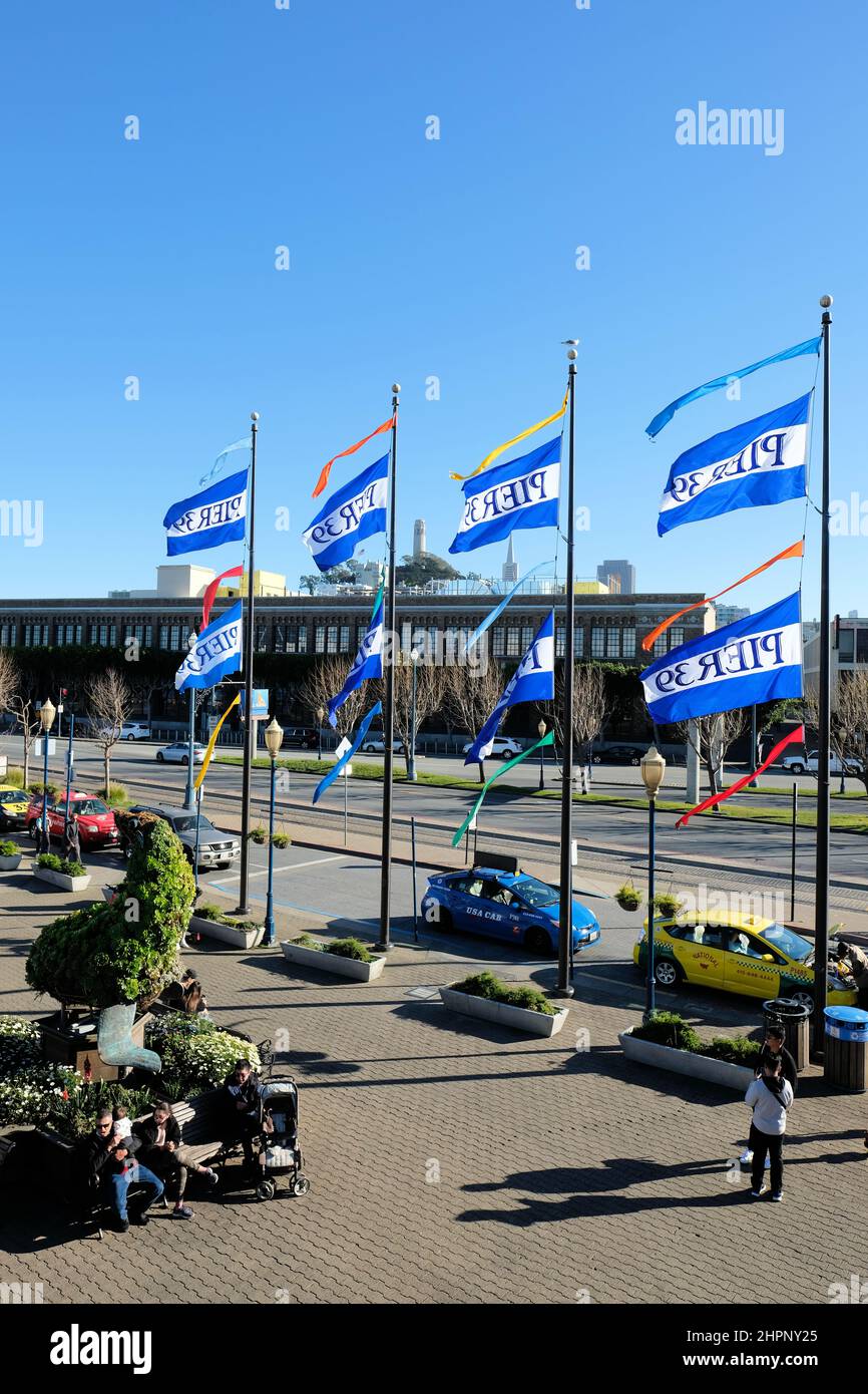 Les drapeaux de l'embarcadère 39 soufflent dans le vent lors d'une journée ensoleillée avec un ciel dégagé ; Coit Tower et Transamerica Building dans les gratte-ciel ; San Francisco California, États-Unis. Banque D'Images