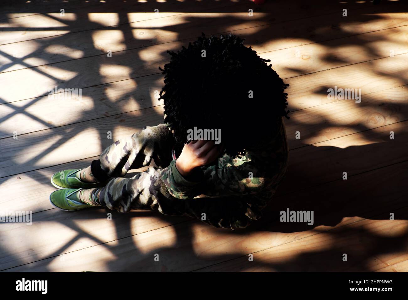 Vue de dessus seule une femme vietnamienne s'assoit à l'intérieur sur un sol en bois avec ombre portée de la porte par après-midi ensoleillé, les gens portent des vêtements de soldat et des cheveux rouillés Banque D'Images