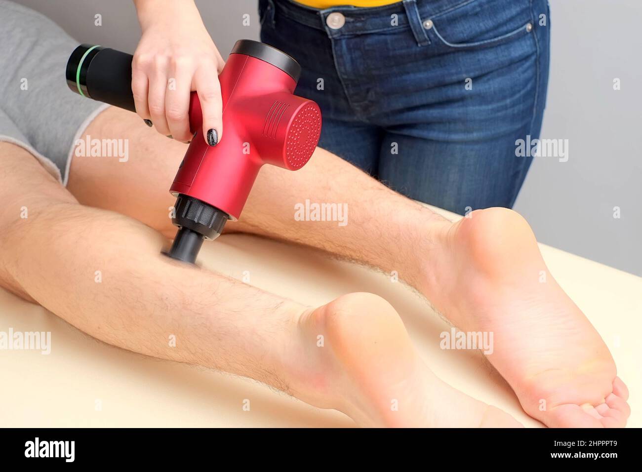 Masseuse femelle massante les muscles du mollet d'un sportif avec masseur à percussion Banque D'Images