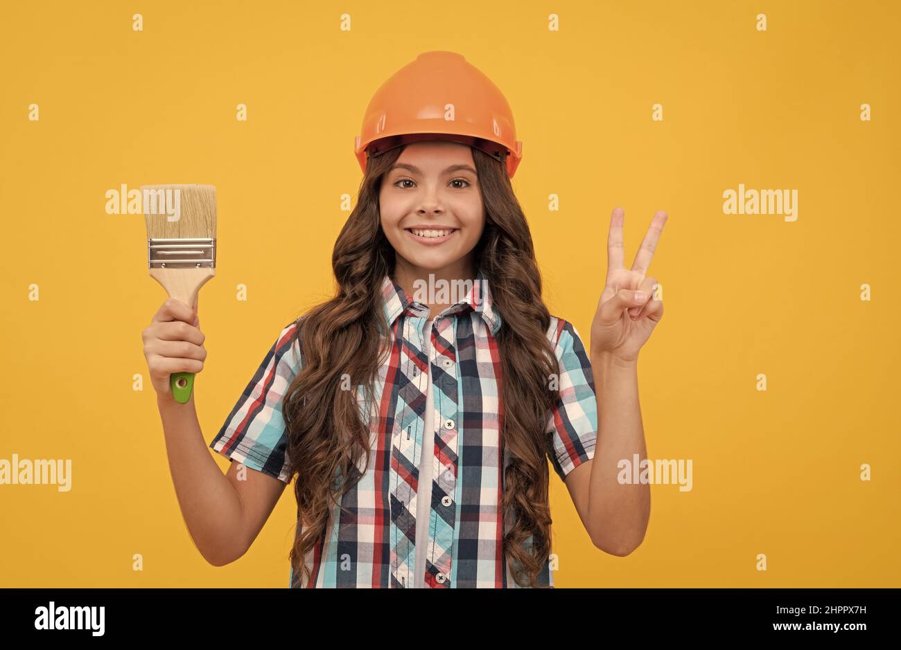 bonne adolescente dans la construction casque tenir la peinture brosse montrer la paix geste, la décoration. Banque D'Images