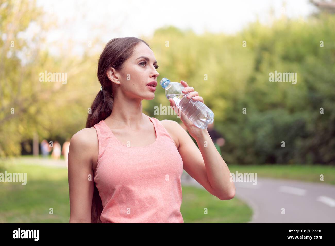 Femme sportive debout piste de course dans le parc d'été boire de l'eau après des exercices de course femelle caucasienne séance d'entraînement matinale jogging sain style de vie co Banque D'Images