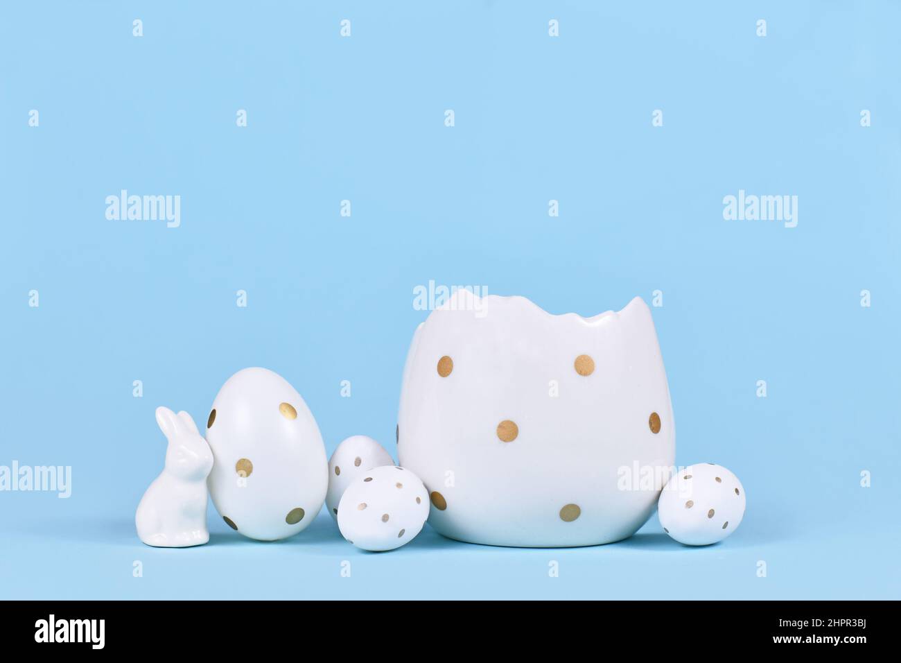 Œufs de pâques blancs à pois dorés, figurine de lapin et coquetier sur fond bleu avec espace pour copier Banque D'Images