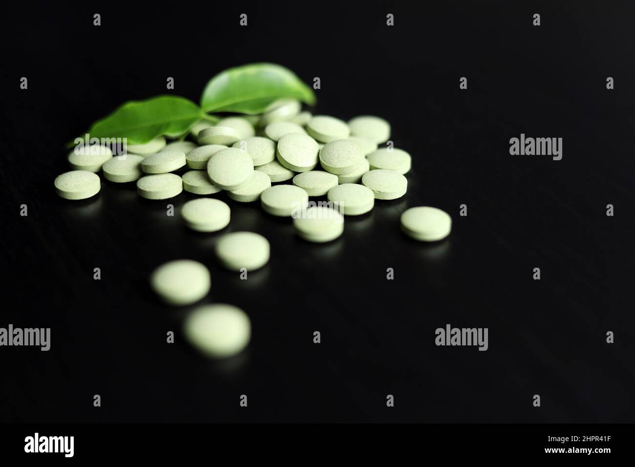 Pilules vertes avec feuilles dispersées sur une table en bois sombre. Médicaments à base de plantes, surnourriture pour la santé Banque D'Images