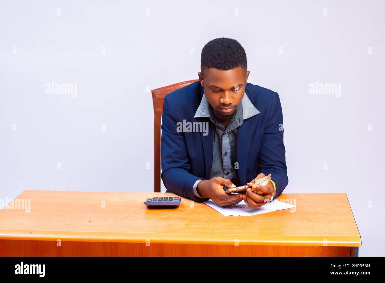 Le beau homme d'affaires africain calcule ses dépenses à l'aide d'une calculatrice Banque D'Images