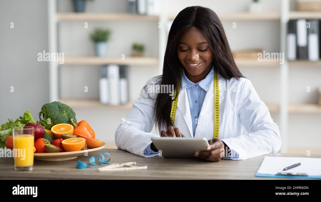 Jeune diététicienne blck travaillant avec un ordinateur de tablette, donnant la consultation en ligne ou la création d'un plan de régime au bureau Banque D'Images