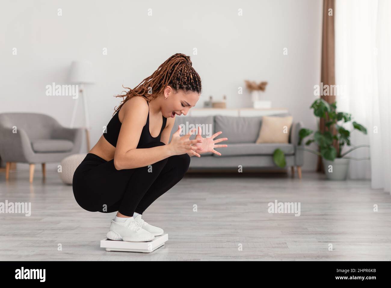 Une femme de fitness malheureuse debout sur des balances criant de pesée à la maison Banque D'Images