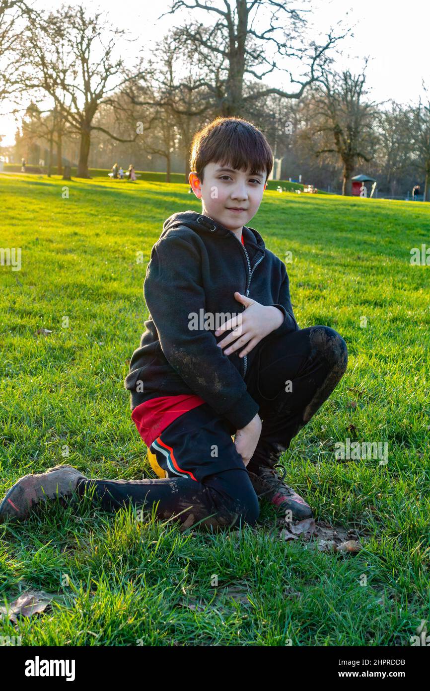 Un garçon s'assoit sur un ballon de football et se repose au milieu d'un parc en février à Reading, au Royaume-Uni Banque D'Images