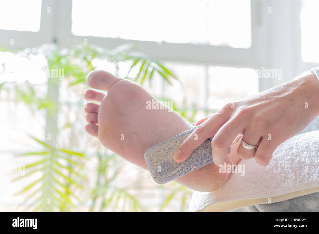 mains d'une jeune femme utilisant une pierre ponce pour adoucir les calloses sur ses pieds. concept soins du corps, pédicure et réflexologie des pieds Banque D'Images