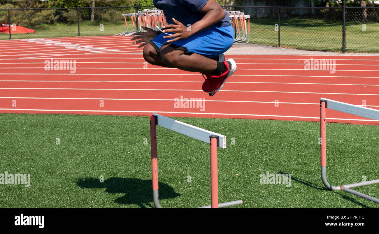 Un jeune Africain américain, dans les airs, sautant sur une piste, un obstacle sur un terrain de gazon au camp d'été d'avant-saison. Banque D'Images