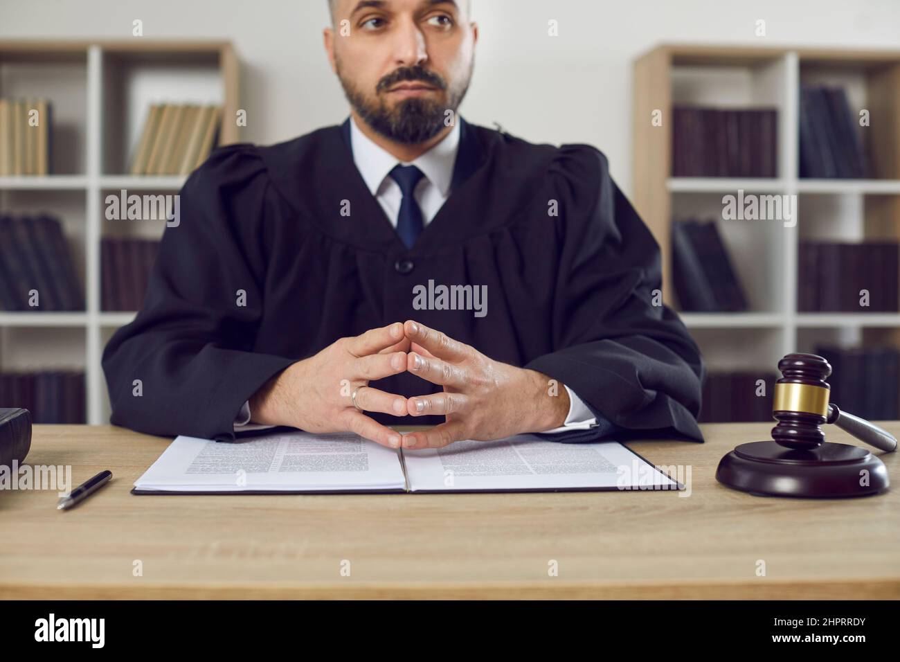 Jeune juge masculin assis à sa table pendant une audience de procès au palais de justice Banque D'Images