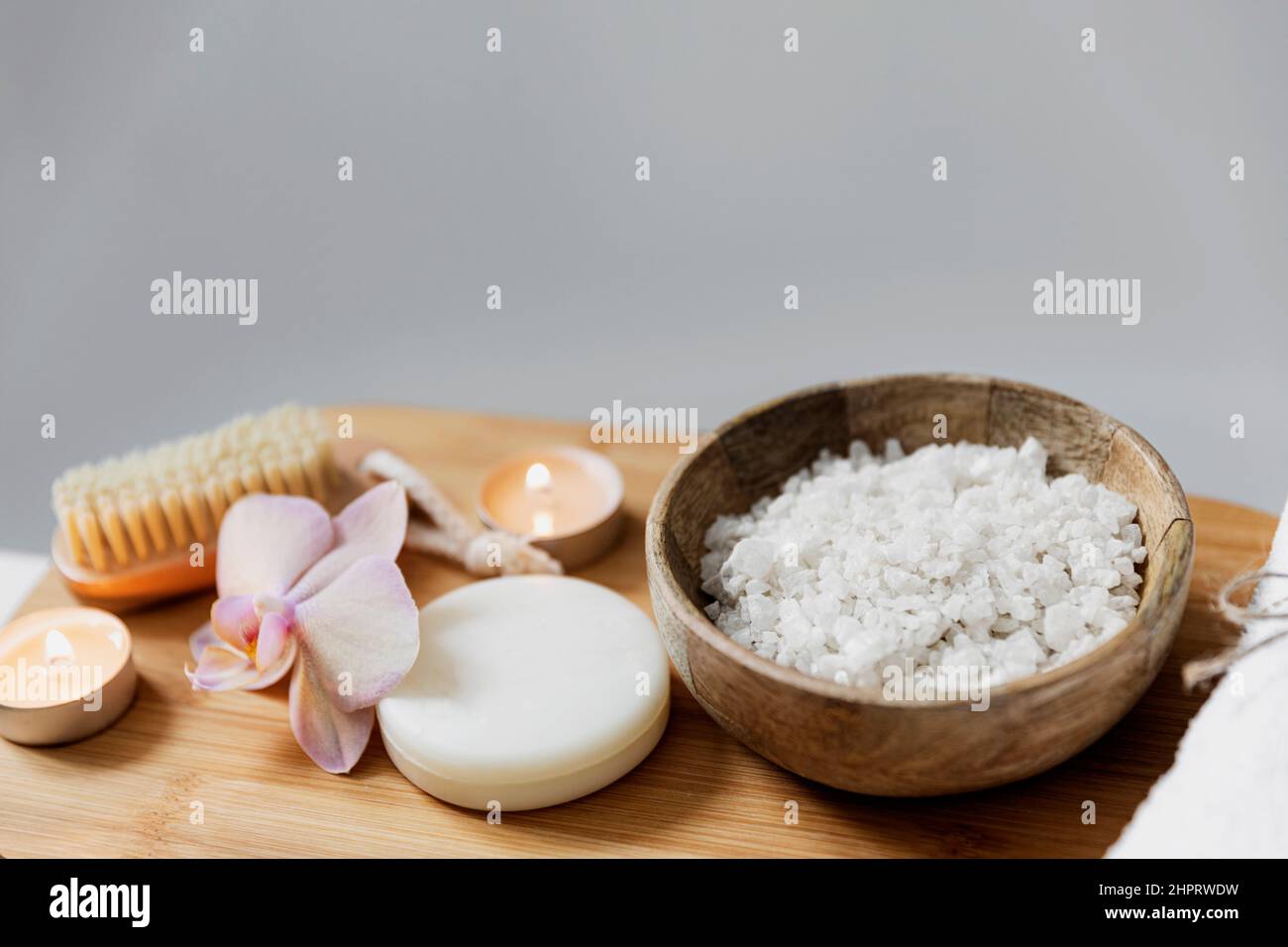 Préparation pour le traitement de spa de l'hôtel ou la procédure de bain à la maison. Lavabo blanc dans la salle de bains avec accessoires sur le plateau. Bougies allumées, débarbouillette, savon, brosse à pied, bouteille avec sel de mer, fleur d'orchidée Banque D'Images