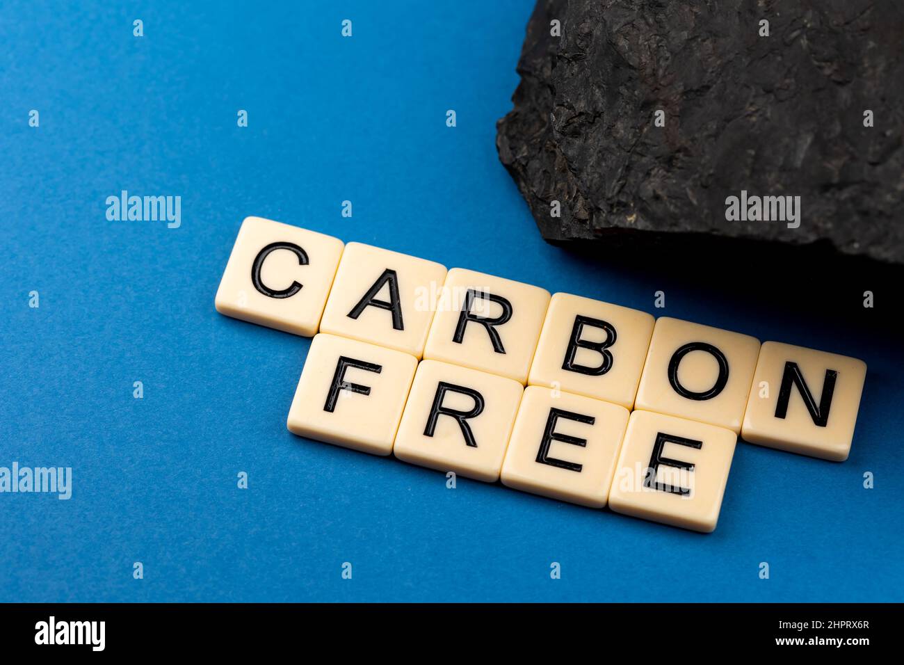 Un morceau de charbon disposé sur fond bleu avec la phrase "sans carbone" composée de lettres. Photo prise sous une lumière artificielle douce Banque D'Images