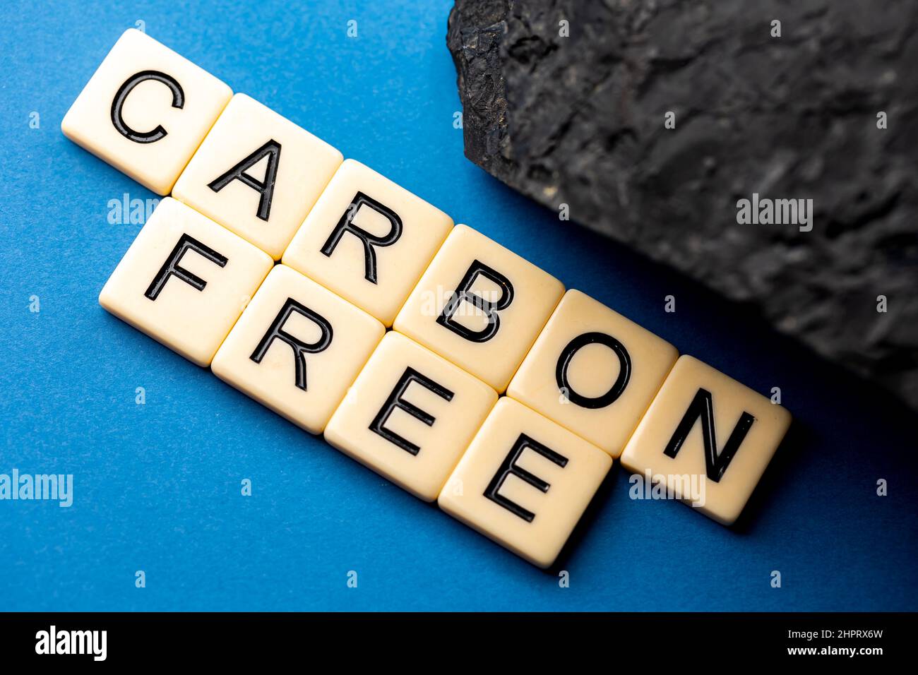 Un morceau de charbon disposé sur fond bleu avec la phrase "sans carbone" composée de lettres. Photo prise sous une lumière artificielle douce Banque D'Images