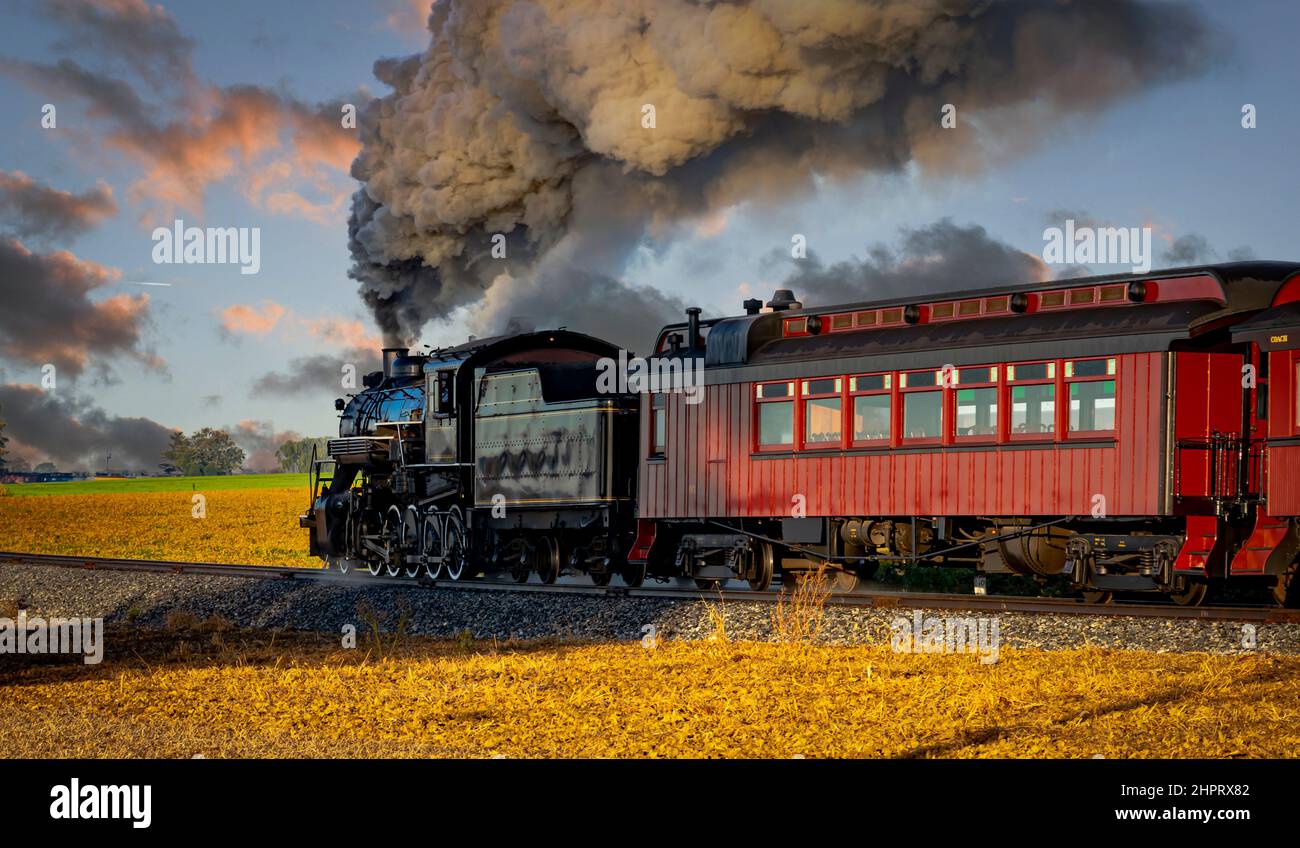 Une vue sur un train à vapeur pour passagers anciens qui dégage de la fumée au lever du soleil lors d'une belle journée partiellement nuageux Banque D'Images