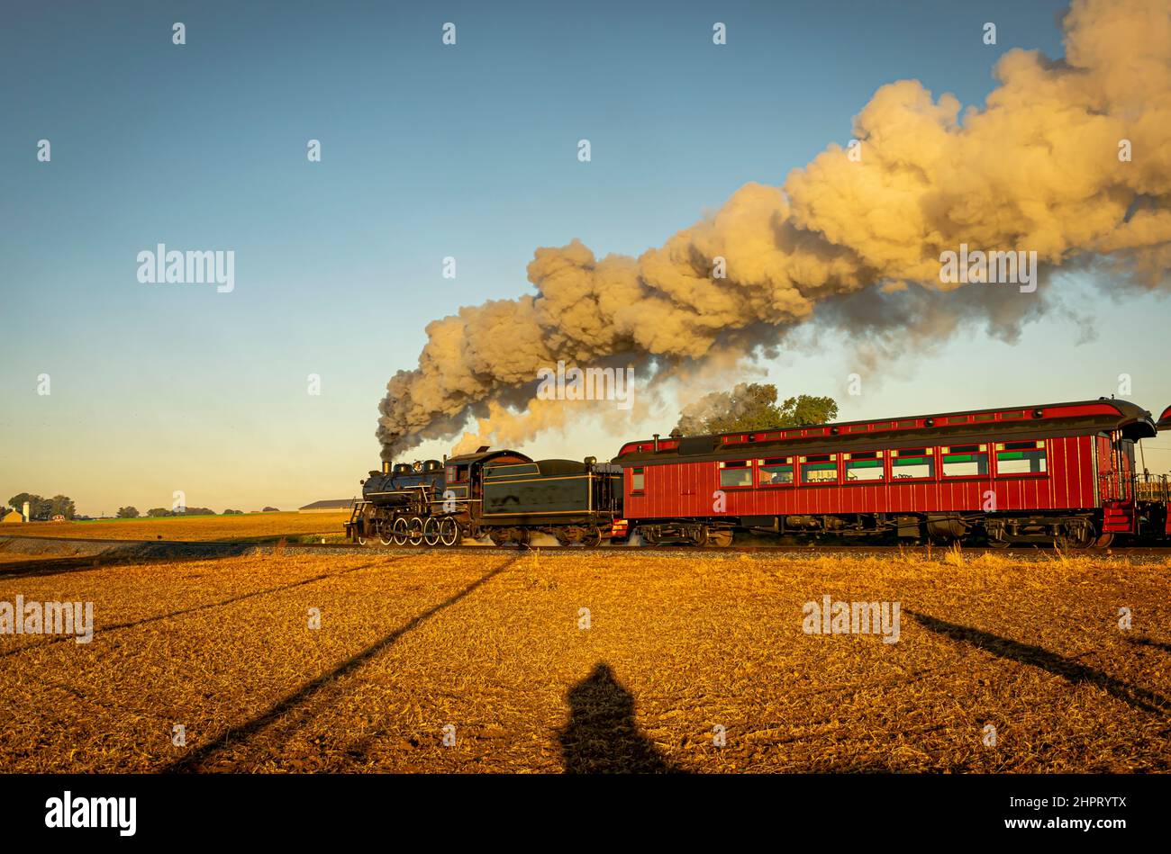 Une vue sur un train à vapeur pour passagers anciens qui soufflait de fumée passe de voyage au lever du soleil lors d'une belle journée sans nuages Banque D'Images