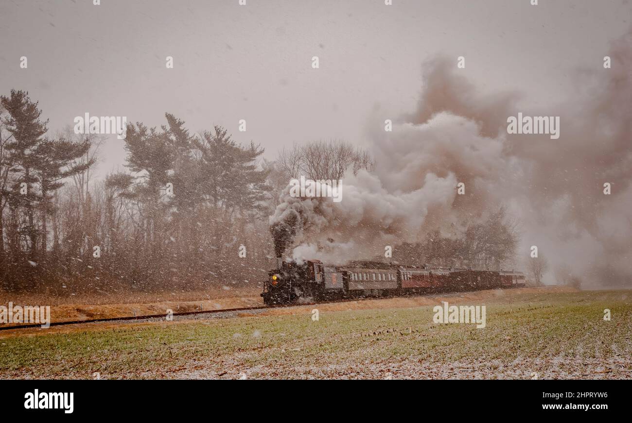Vue d'un train de passagers à vapeur antique voyageant dans une tempête de neige qui vient de commencer une journée d'hiver Banque D'Images