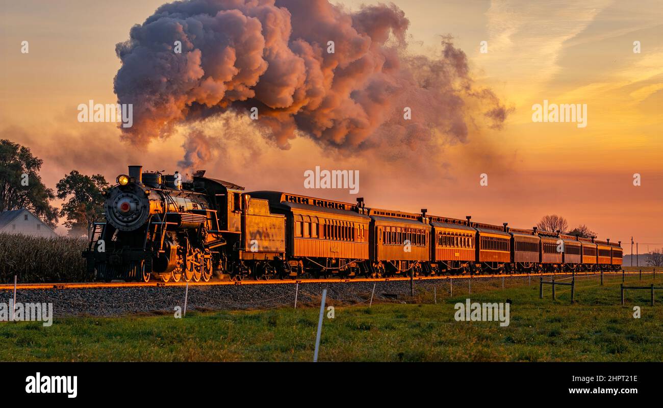 Vue sur un train de passagers à vapeur antique qui s'approche à Sunrise avec une tête de vapeur et de fumée qui se déplace à travers les terres agricoles Banque D'Images
