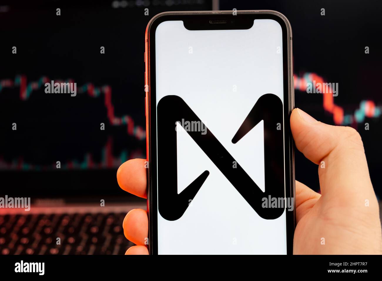 PRÈS du protocole PRÈS du logo de crypto-monnaie sur l'écran du smartphone dans la main des mans avec tendance à la baisse sur la carte sur un fond rouge clair, février 2022, San Francisco, USA. Banque D'Images