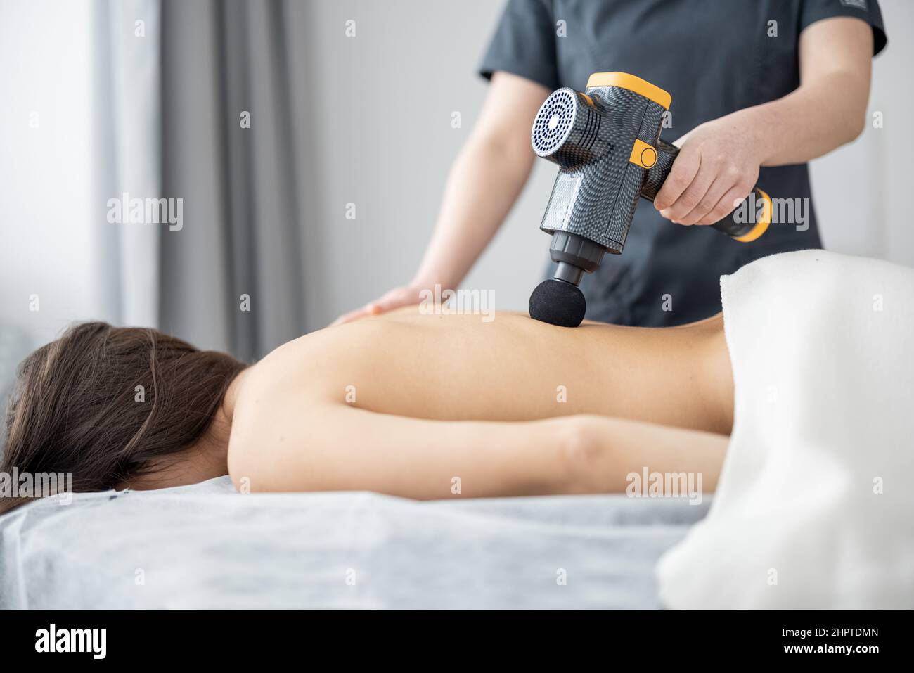 La femme fait un massage du dos du patient à l'aide d'un masseur à percussion Banque D'Images
