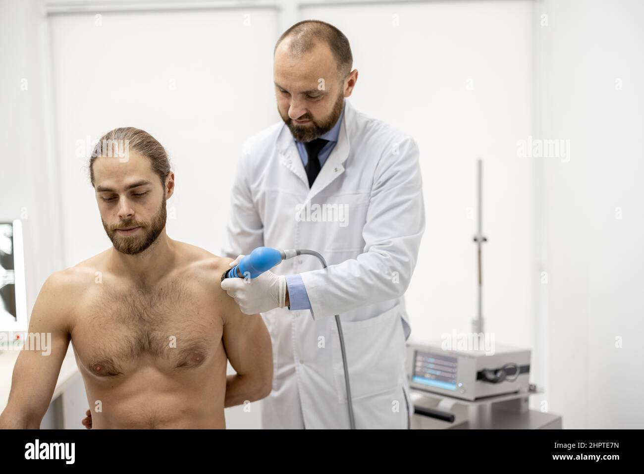 Le médecin applique un traitement par onde de choc sur l'épaule des hommes Banque D'Images