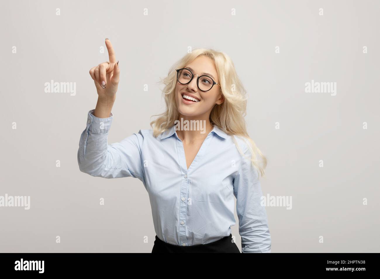 Bonne femme entrepreneur en appuyant sur le bouton sur l'écran virtuel sur fond gris clair de studio, maquette pour le design Banque D'Images