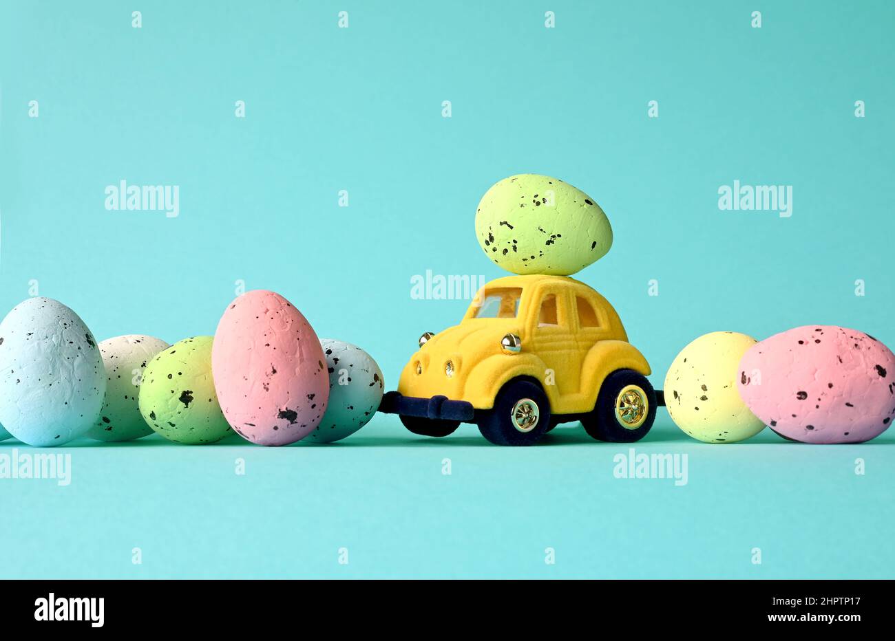 Un œuf de Pâques sur une petite voiture sur fond bleu avec des œufs colorés. Copier l'espace. Carte de Pâques. Banque D'Images