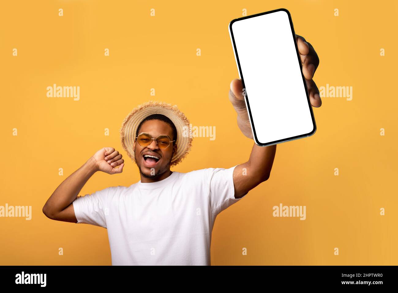 Beau homme noir en lunettes de soleil et chapeau de paille montrant smartphone avec maquette pour la conception d'application mobile ou de site Web Banque D'Images