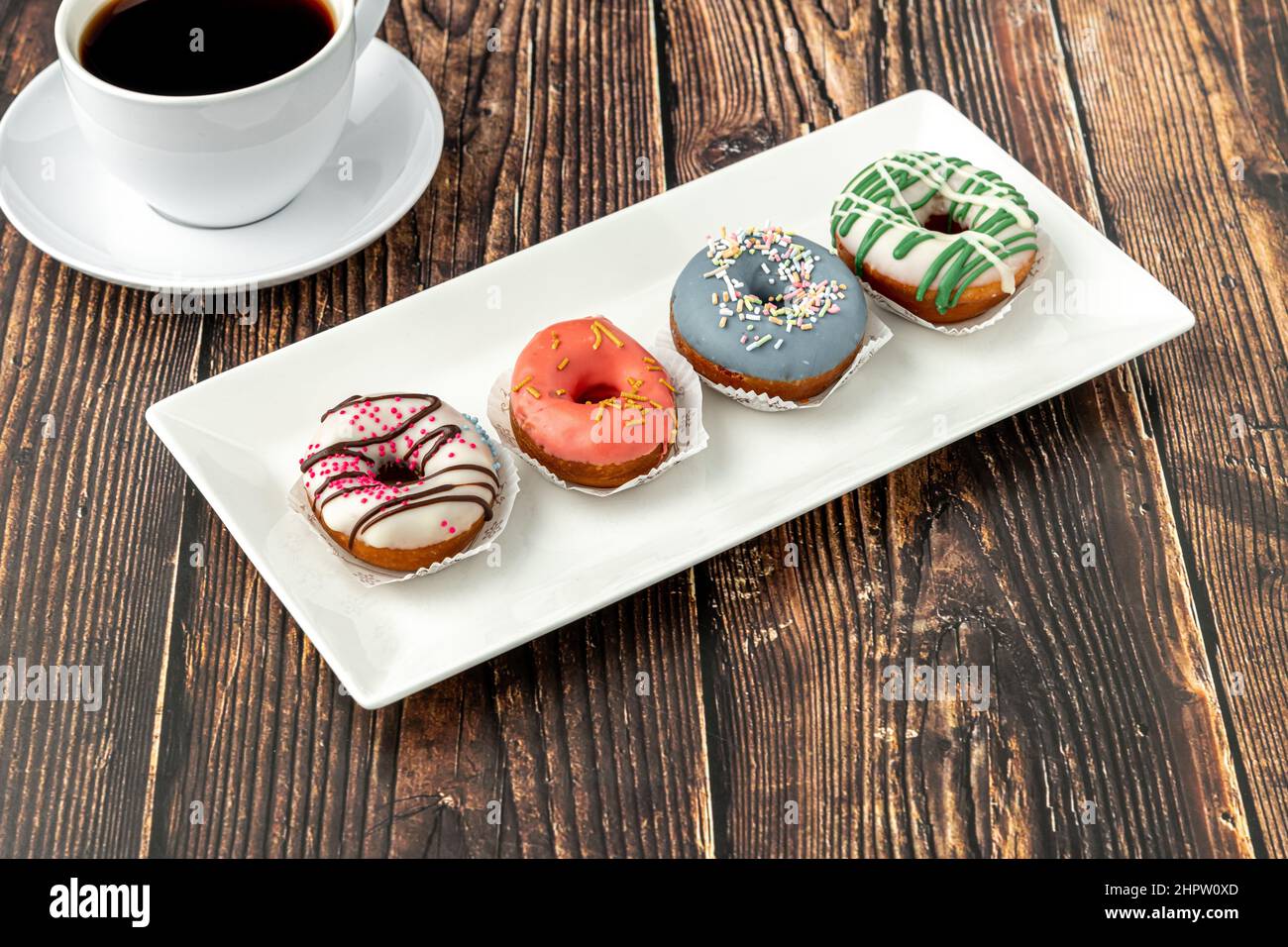 Délicieux mini beignets colorés avec café sur table en bois Banque D'Images