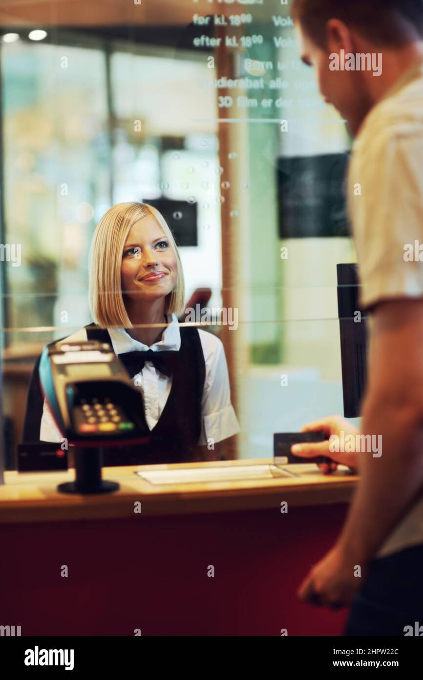 Billet pour deux. Une belle femme habillée en uniforme assise dans une billetterie servant un client masculin. Banque D'Images