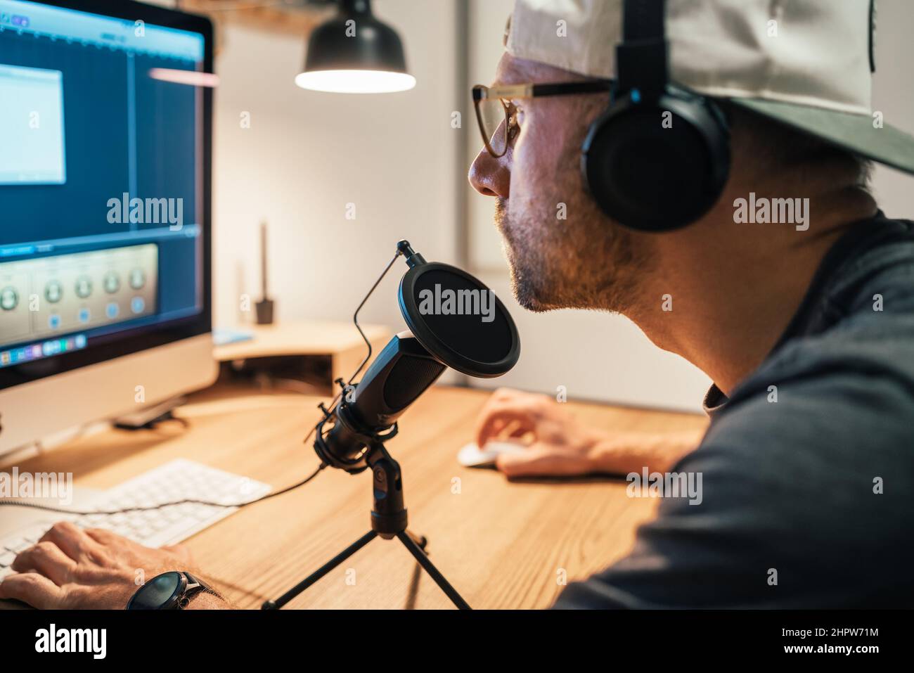 Milieu d'âge dans les casques et le baseball faisant le montage audio vidéo à l'aide d'un ordinateur de bureau avec le logiciel de montage multimédia. Système audio et son moderne Banque D'Images