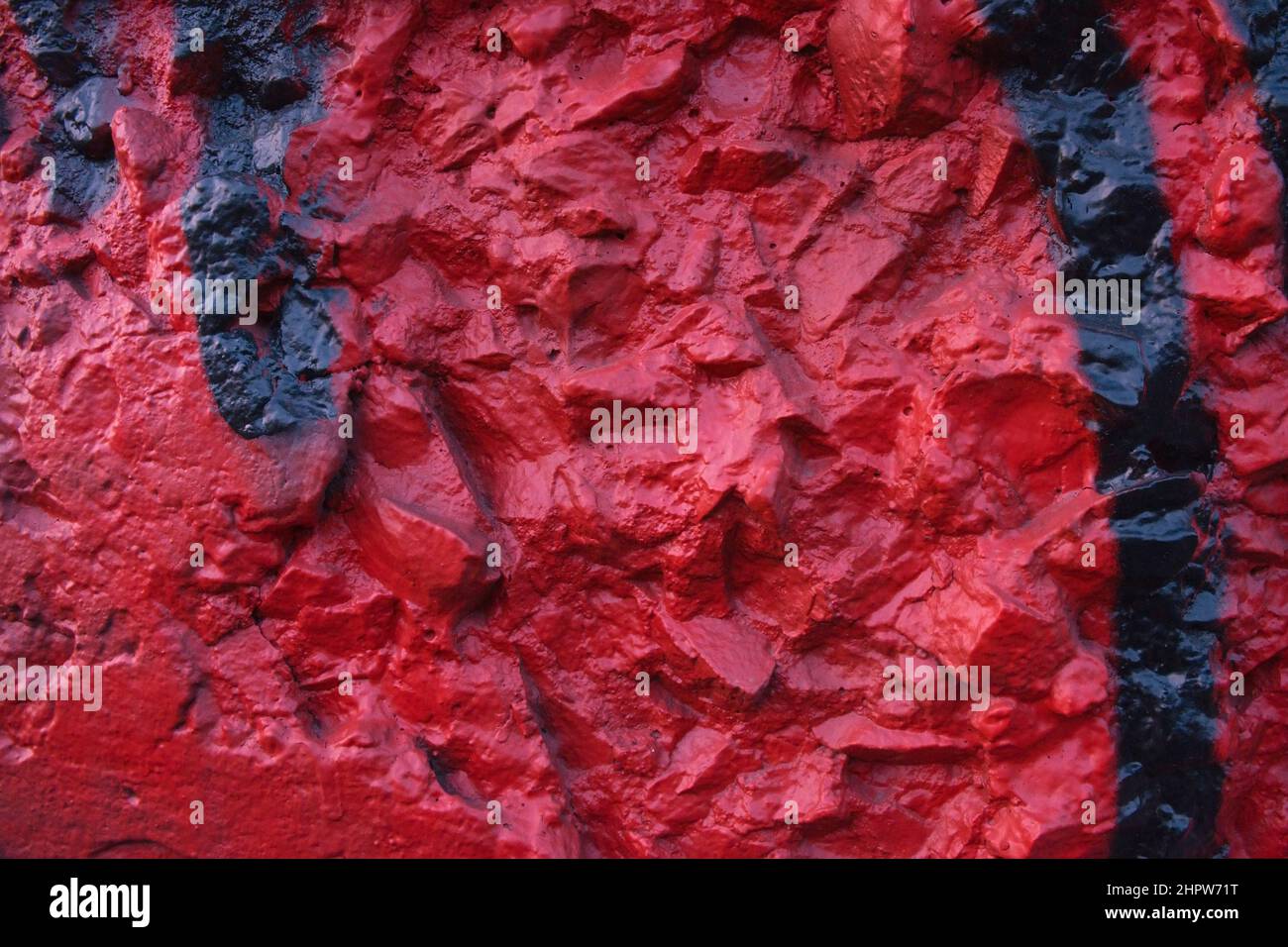 Mur de relief peint en rouge foncé avec éléments convexes chaotiques rugueux. Mur en béton recouvert de stuc décoratif inégal et peinture rouge foncé et noire. Banque D'Images