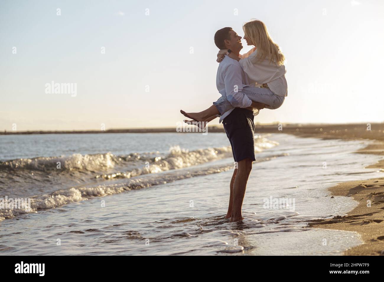 Pleine photo de l'homme tenant la femme dans ses bras debout au bord de la mer Banque D'Images