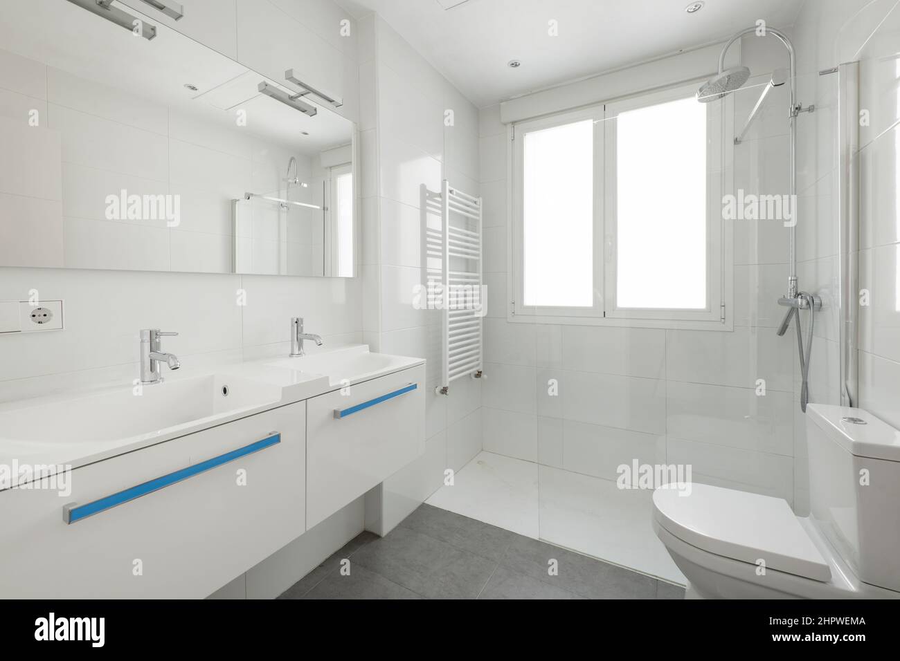 Nouvelle salle de bains avec double lavabo en porcelaine blanche et miroir rectangulaire sans cadre, radiateur pour sécher les serviettes à l'intérieur de la douche et fenêtre en aluminium blanc Banque D'Images