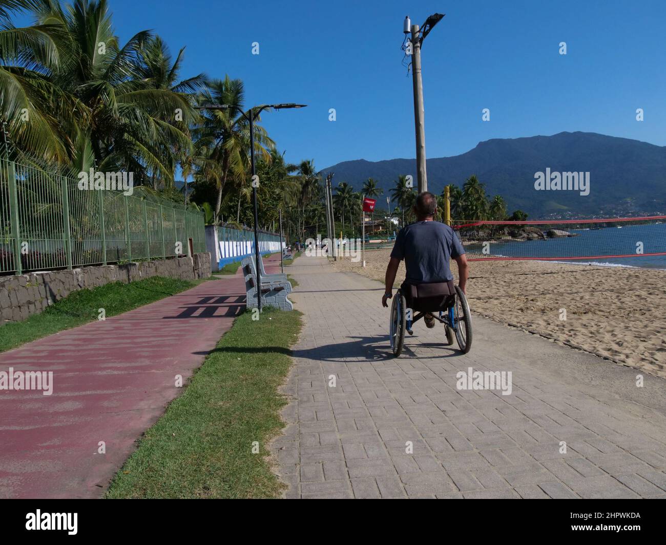 Un homme handicapé en fauteuil roulant s'approche du spectateur. Il utilise la voie piétonne de l'île d'Ilhabela, au Brésil, ce qui est très pratique Banque D'Images