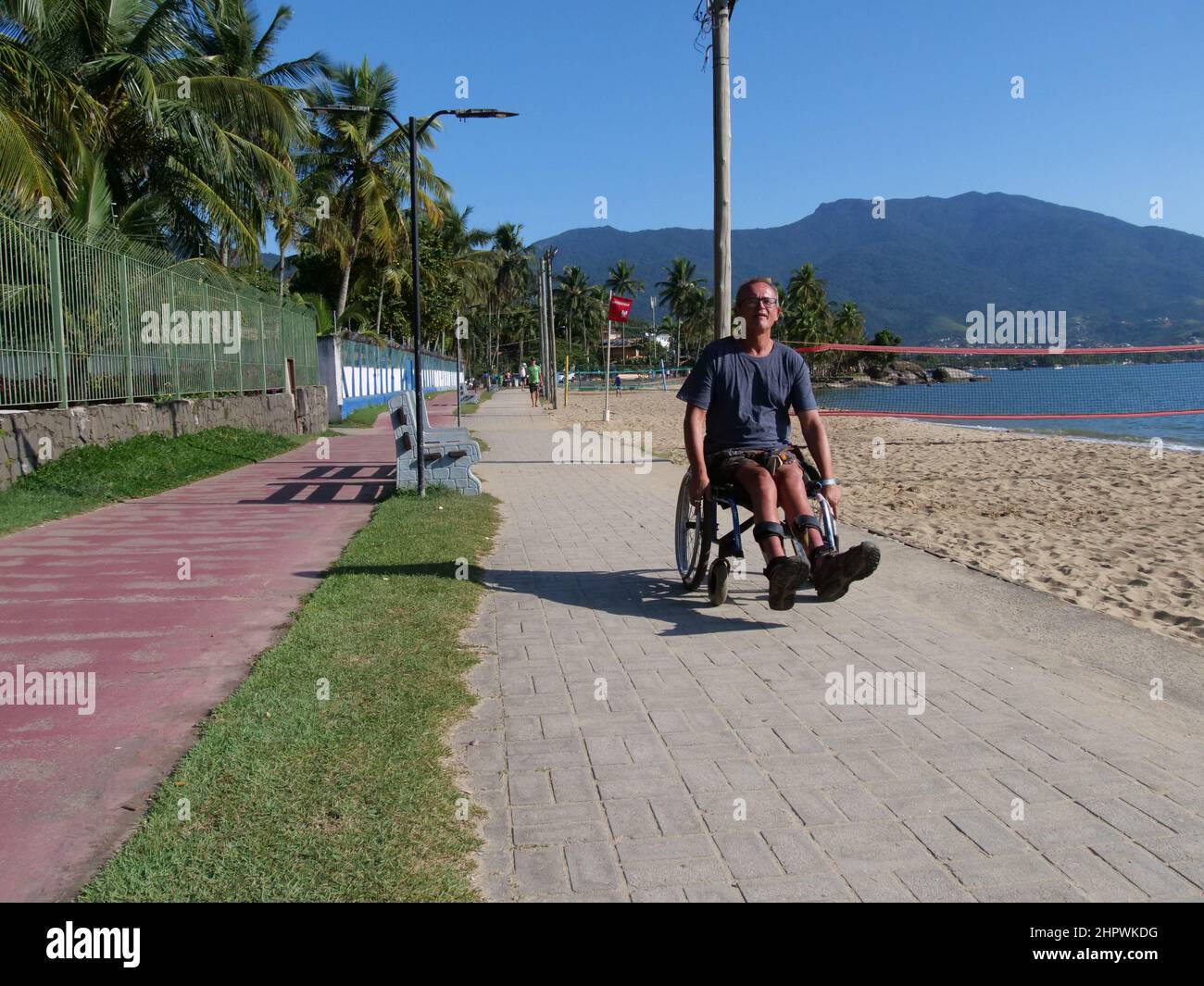 Un homme handicapé en fauteuil roulant s'approche du spectateur. Il utilise la voie piétonne de l'île d'Ilhabela, au Brésil, ce qui est très pratique Banque D'Images
