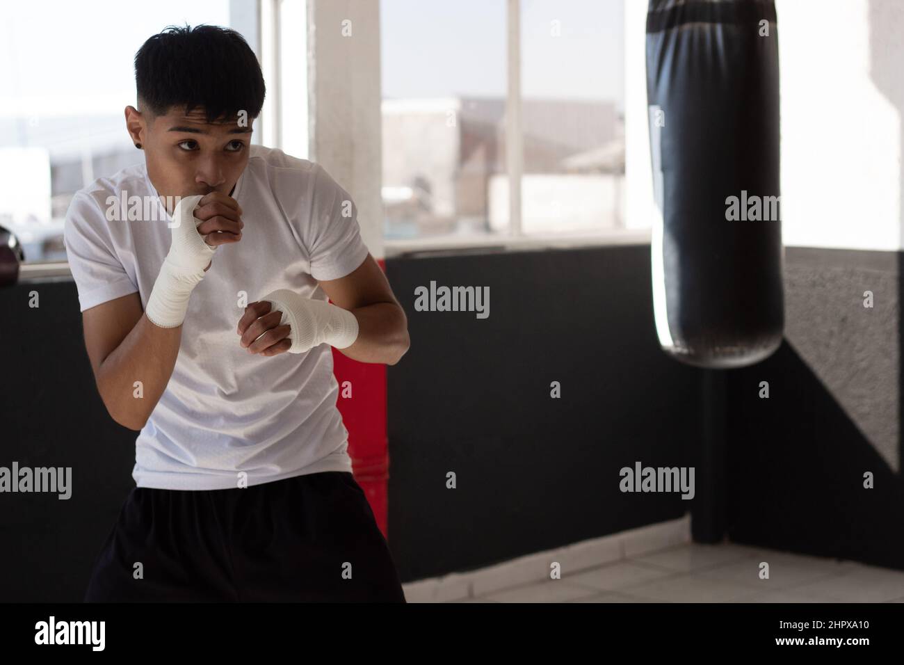 un jeune boxeur portant un t-shirt blanc à l'ombre de boxe avec ses poings bandés pendant son entraînement à l'intérieur de la salle de boxe. Banque D'Images