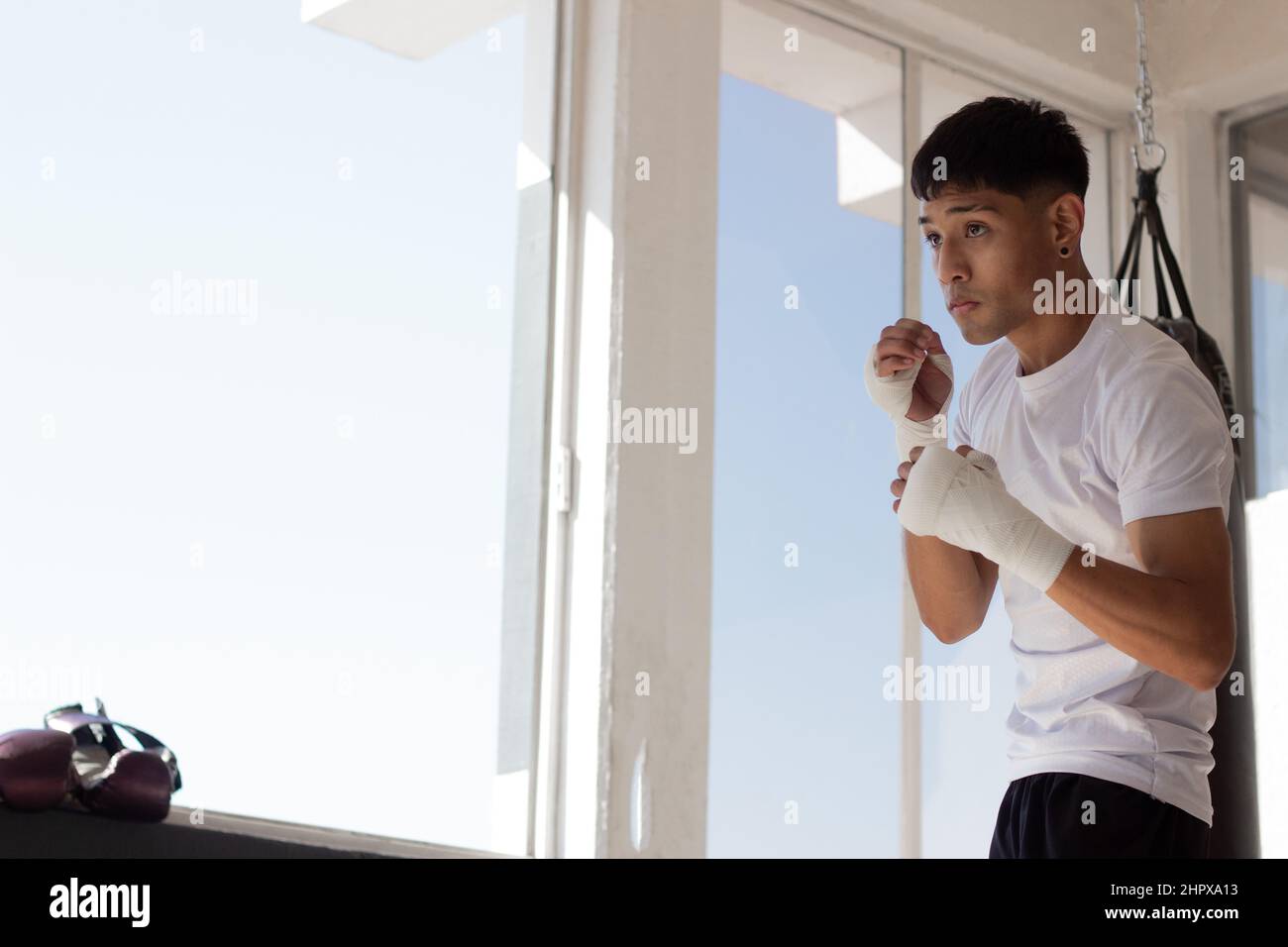 un jeune boxeur portant un t-shirt blanc à l'ombre de boxe avec ses poings bandés pendant son entraînement à l'intérieur de la salle de boxe. Banque D'Images