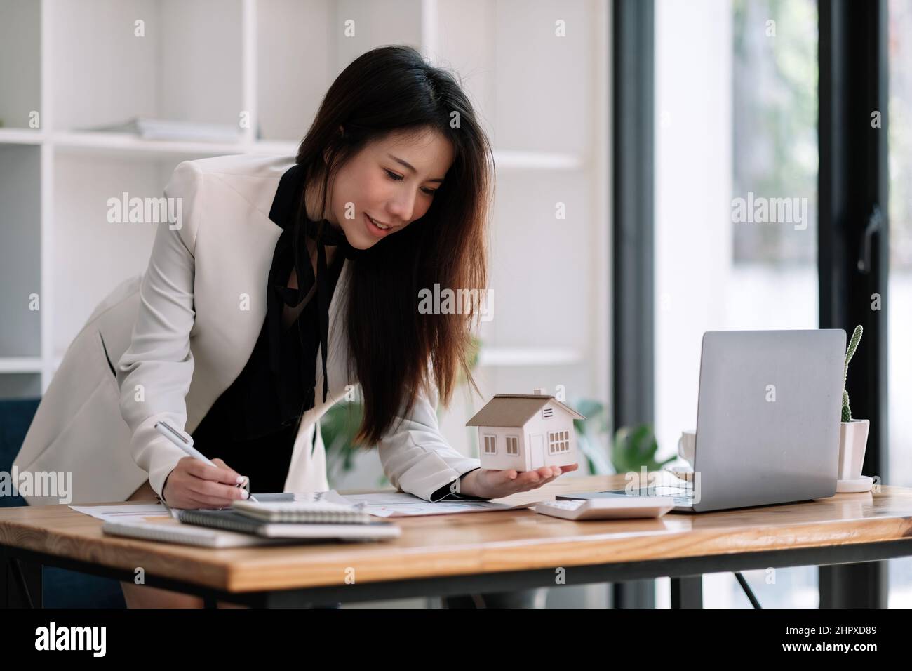 Charmante femme asiatique tenant le modèle de maison en main et calculant le tableau financier pour l'investissement à l'achat de propriété. Banque D'Images