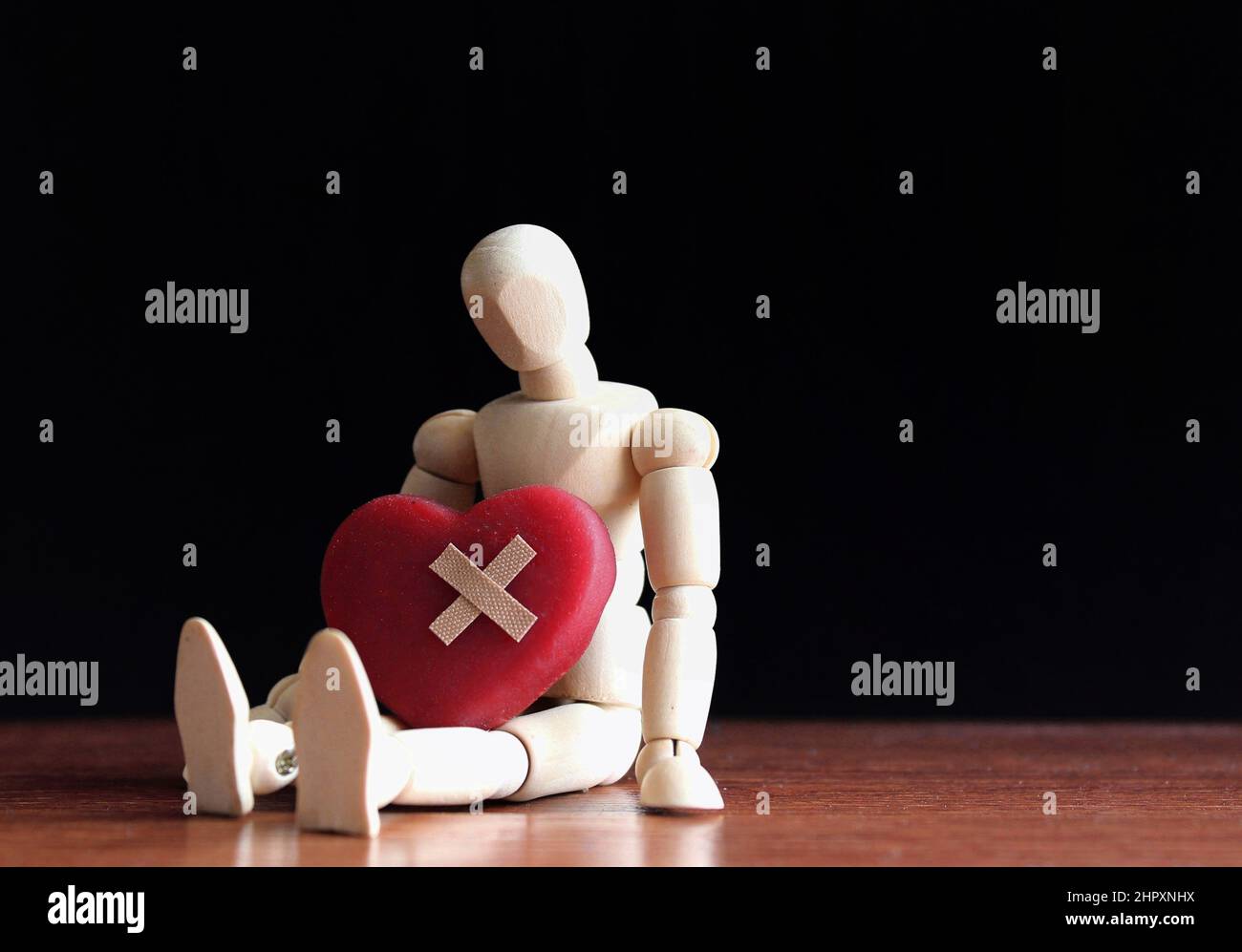 Triste, déchirement et seul concept. Poupée en bois assis dans l'obscurité avec coeur rouge et bandage. Banque D'Images