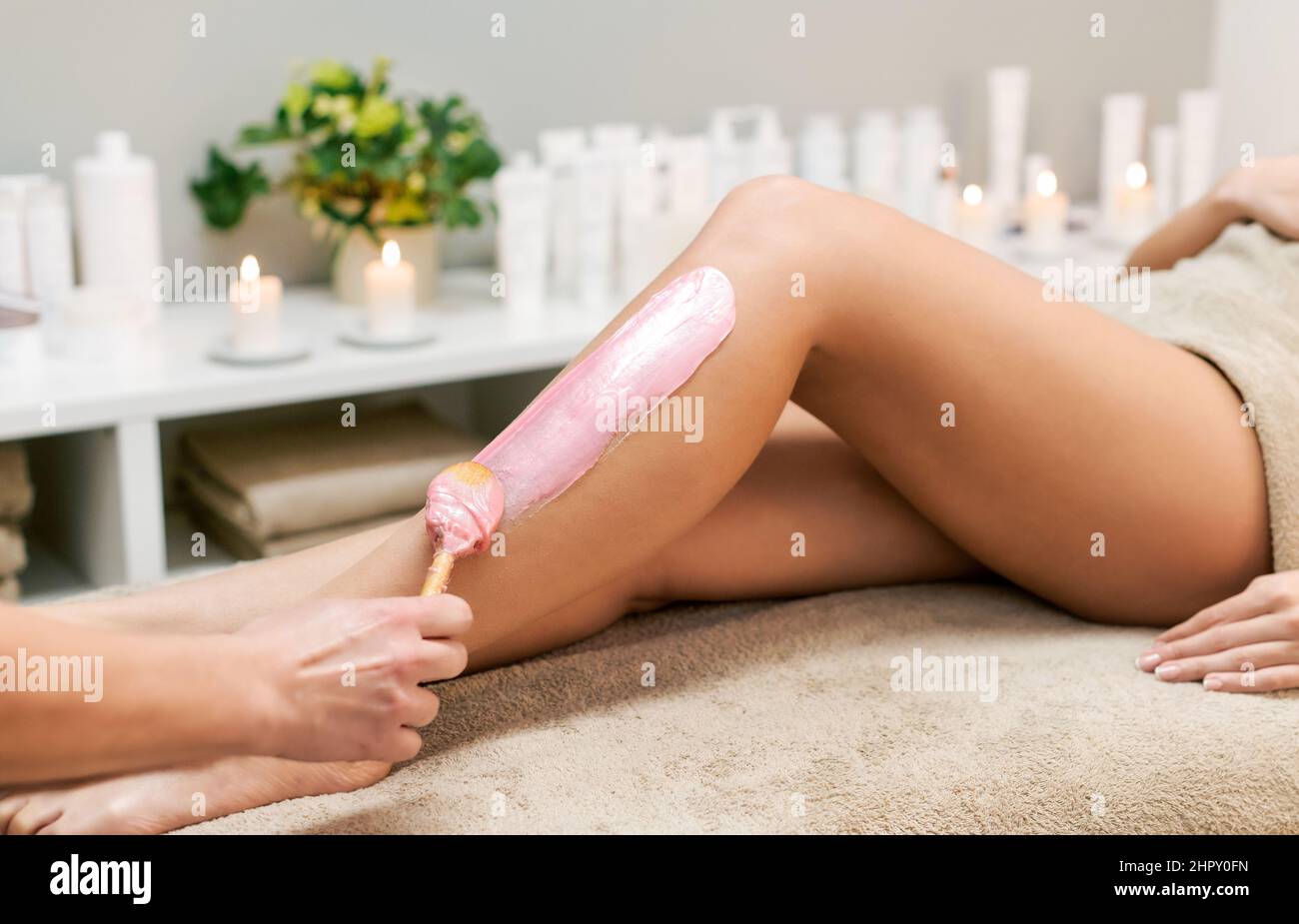 Crop anonyme esthéticienne appliquant de la cire rose sur la jambe de la femme sans visage client pendant la procédure d'épilation dans un salon de spa moderne et léger Banque D'Images