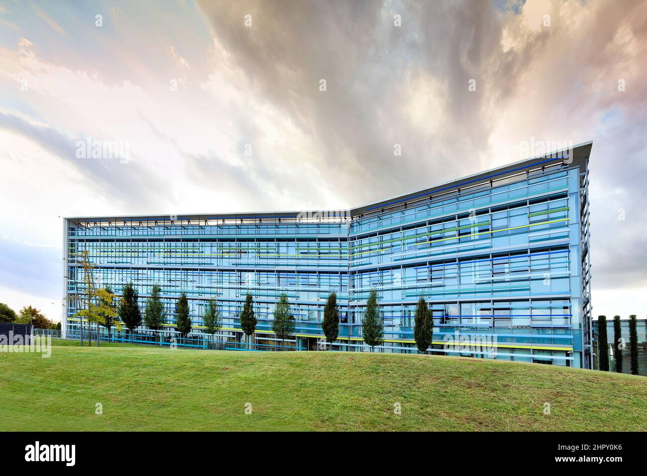 Extérieur du centre d'affaires contemporain en verre au design moderne situé sur une pelouse herbeuse près des arbres de la ville, dans un ciel nuageux Banque D'Images