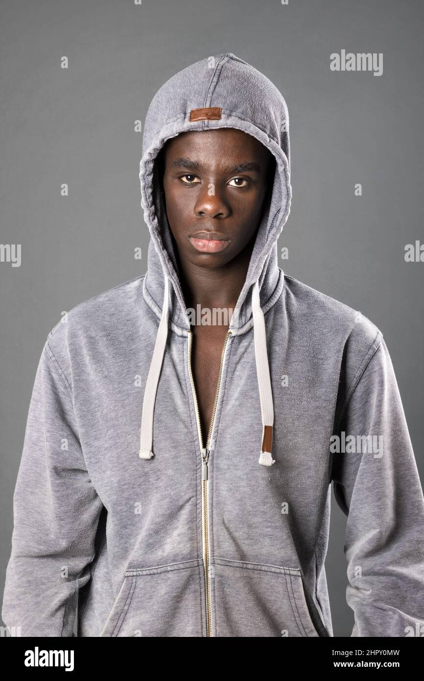Homme afro-américain sérieux à capuche debout et regardant l'appareil photo sur fond gris en studio Banque D'Images
